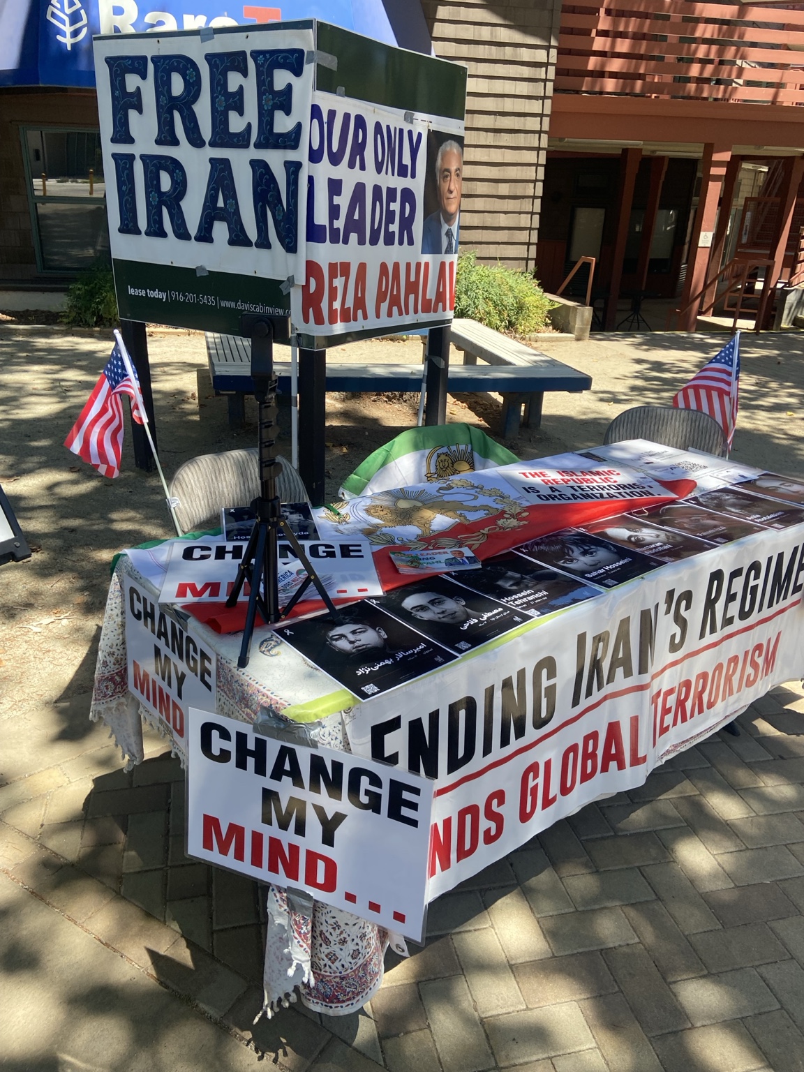 SF Protests Change My Mind information table with educational materials, American flags, and Iran advocacy signs at UC Davis